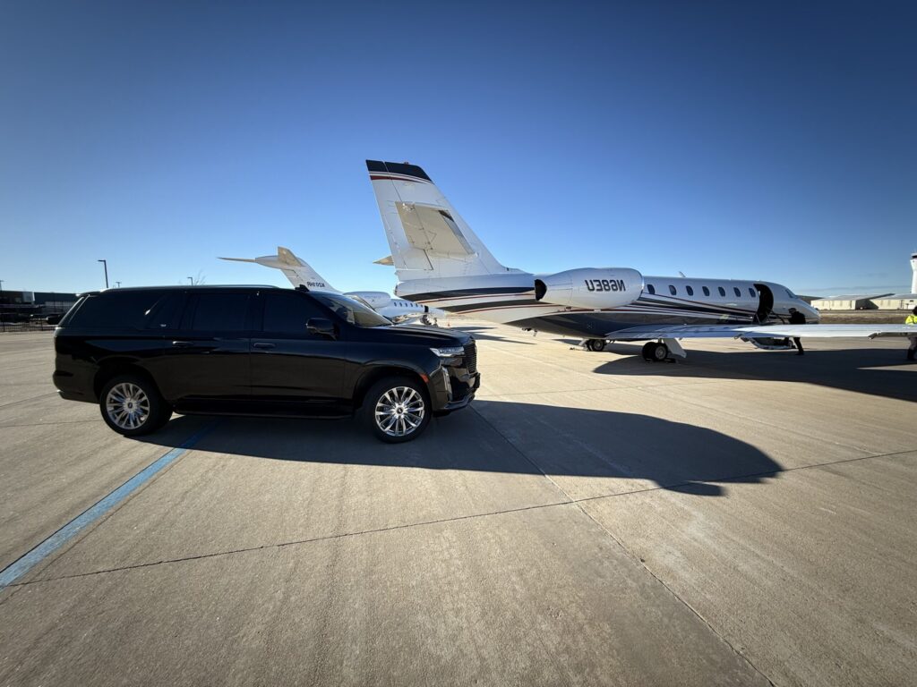 Black Cadillac Escalade SUV parked on an airport tarmac beside private jets